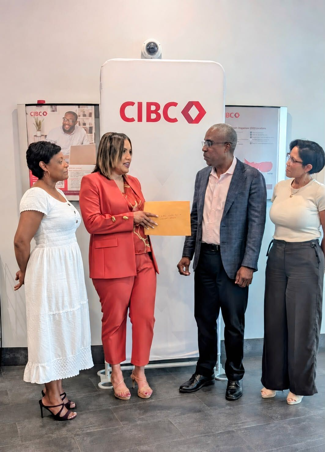 Four people gathered around a presentation envelope in front of a CIBC banner.